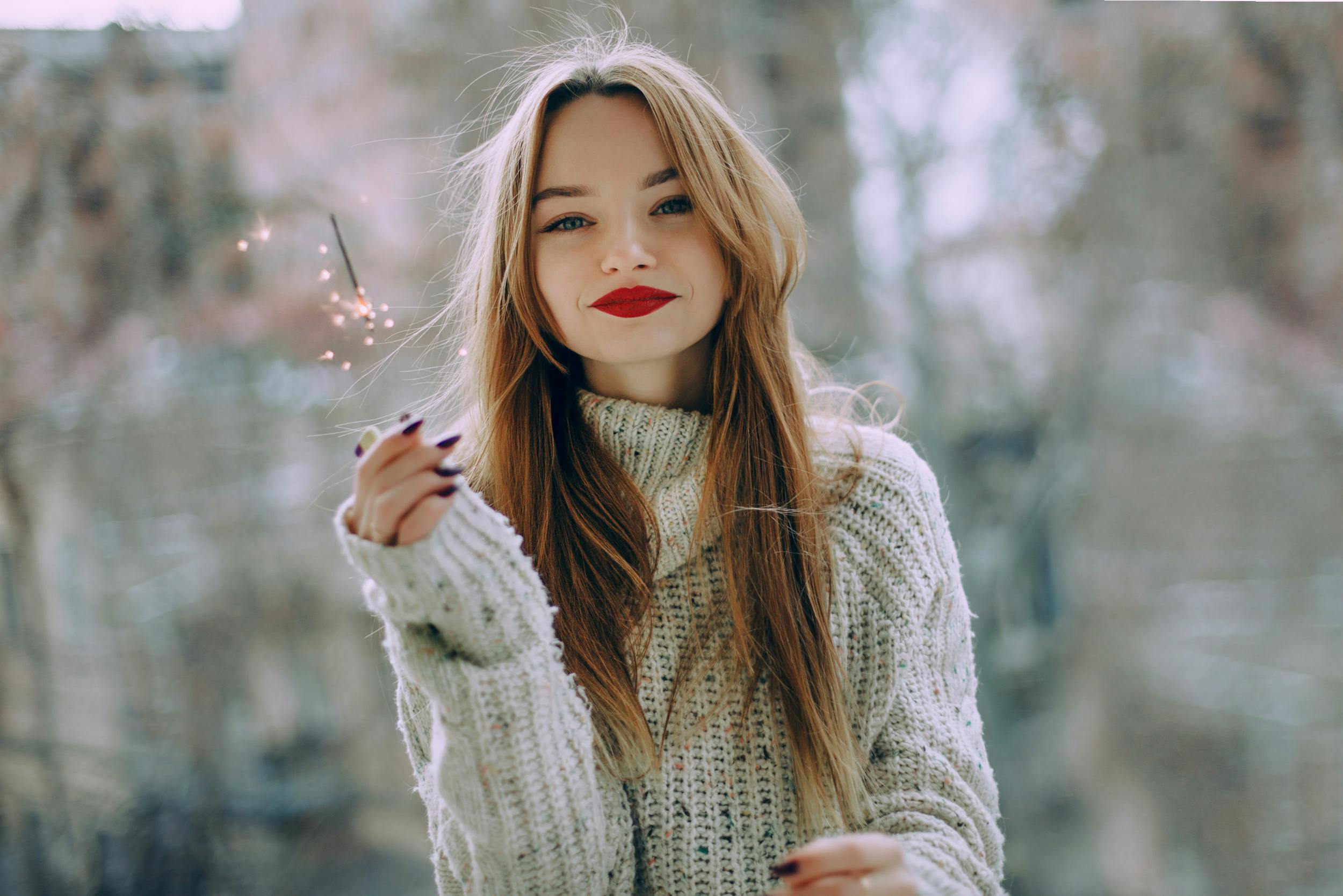 Portrait of a young woman with long hair and red lips holding a sparkler outdoors in Baku.